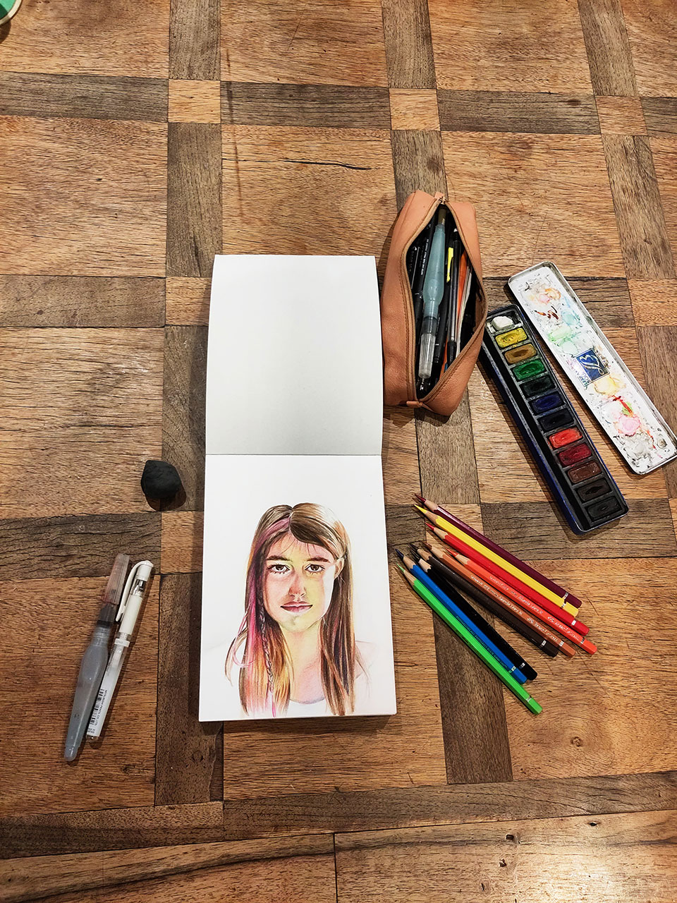 Vue d'un bloc de dessin et de crayons et aquarelle pour le Portrait à l'aquarelle d'une jeune filleau cheveux longs et une tresse rose